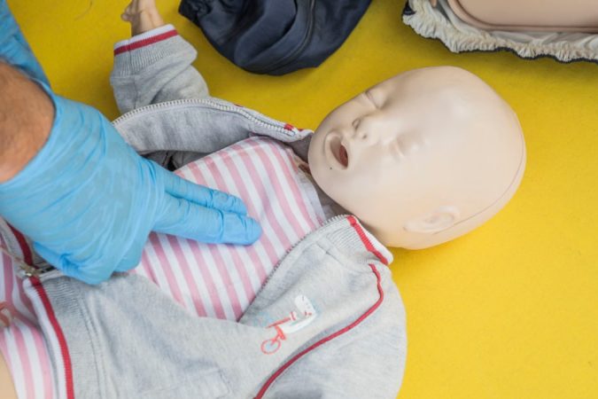 A person demonstrates infant CPR on a manikin, highlighting first aid techniques.