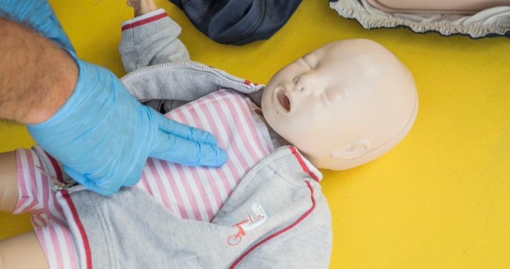 A person demonstrates infant CPR on a manikin, highlighting first aid techniques.
