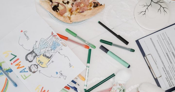 A colorful child's drawing of a family alongside pizza and pens on a table.