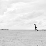 A person running across an expansive desert under a cloudy sky in Natal, Brazil.