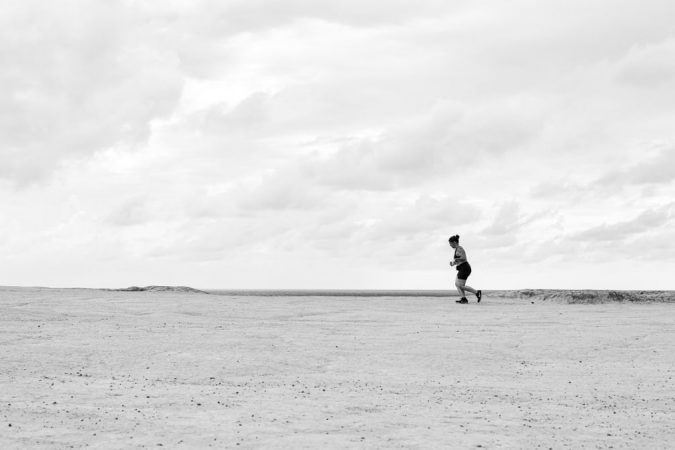 A person running across an expansive desert under a cloudy sky in Natal, Brazil.