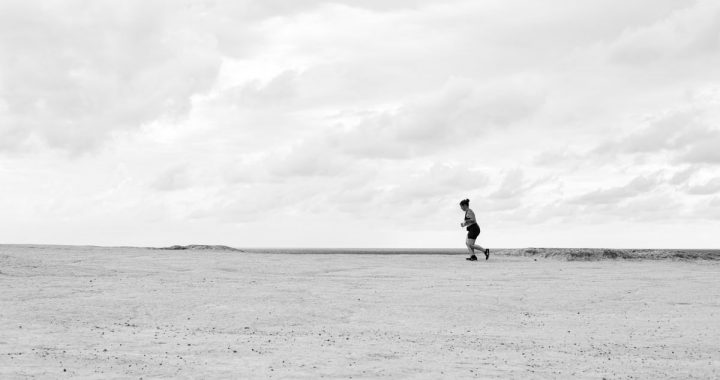 A person running across an expansive desert under a cloudy sky in Natal, Brazil.