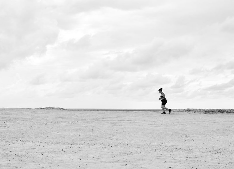 A person running across an expansive desert under a cloudy sky in Natal, Brazil.